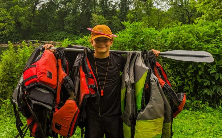 a student carries life jackets hanging on a paddle on a canoeing trip near DC